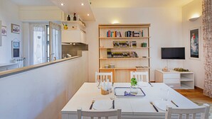 A modern kitchen with white cabinets, a dining table set for four, and a bookshelf filled with books and decorative items. - Cozy Lighthouse Apartment by Wonderful Italy (Santa Margherita Ligure)