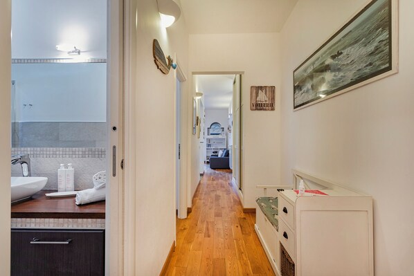 A narrow hallway with a wooden floor leading to a living area with a sofa and a painting.