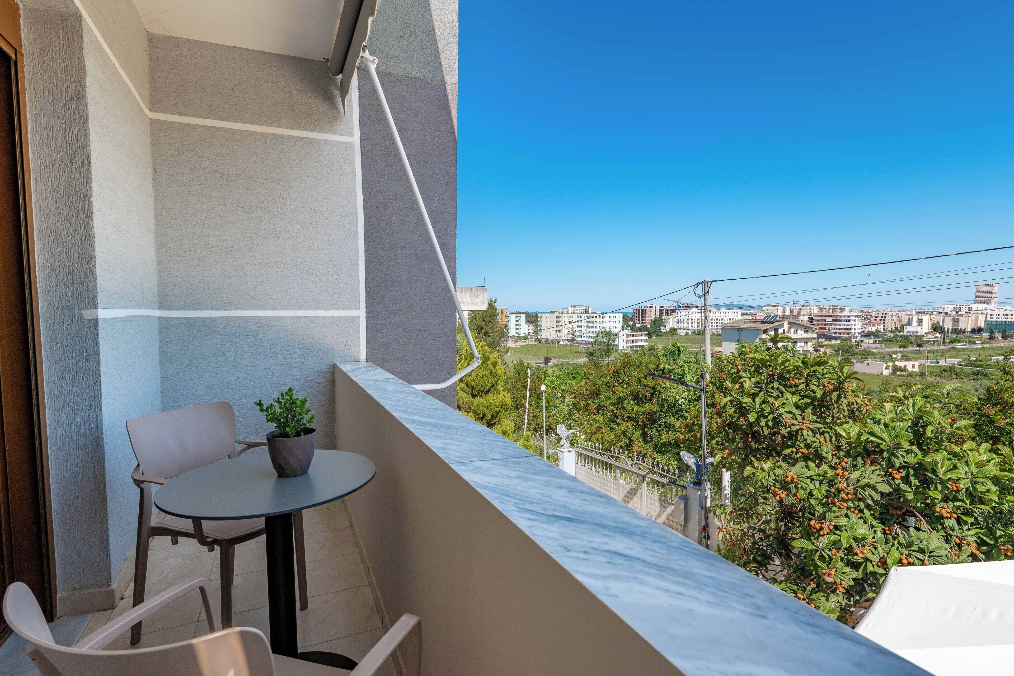 Un balcón con mesa y sillas, con vistas a un paisaje urbano y zonas verdes.