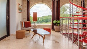 Un interior moderno con una escalera de caracol, un conjunto de sofás, una mesa y un amplio ventanal con vistas a zonas verdes.