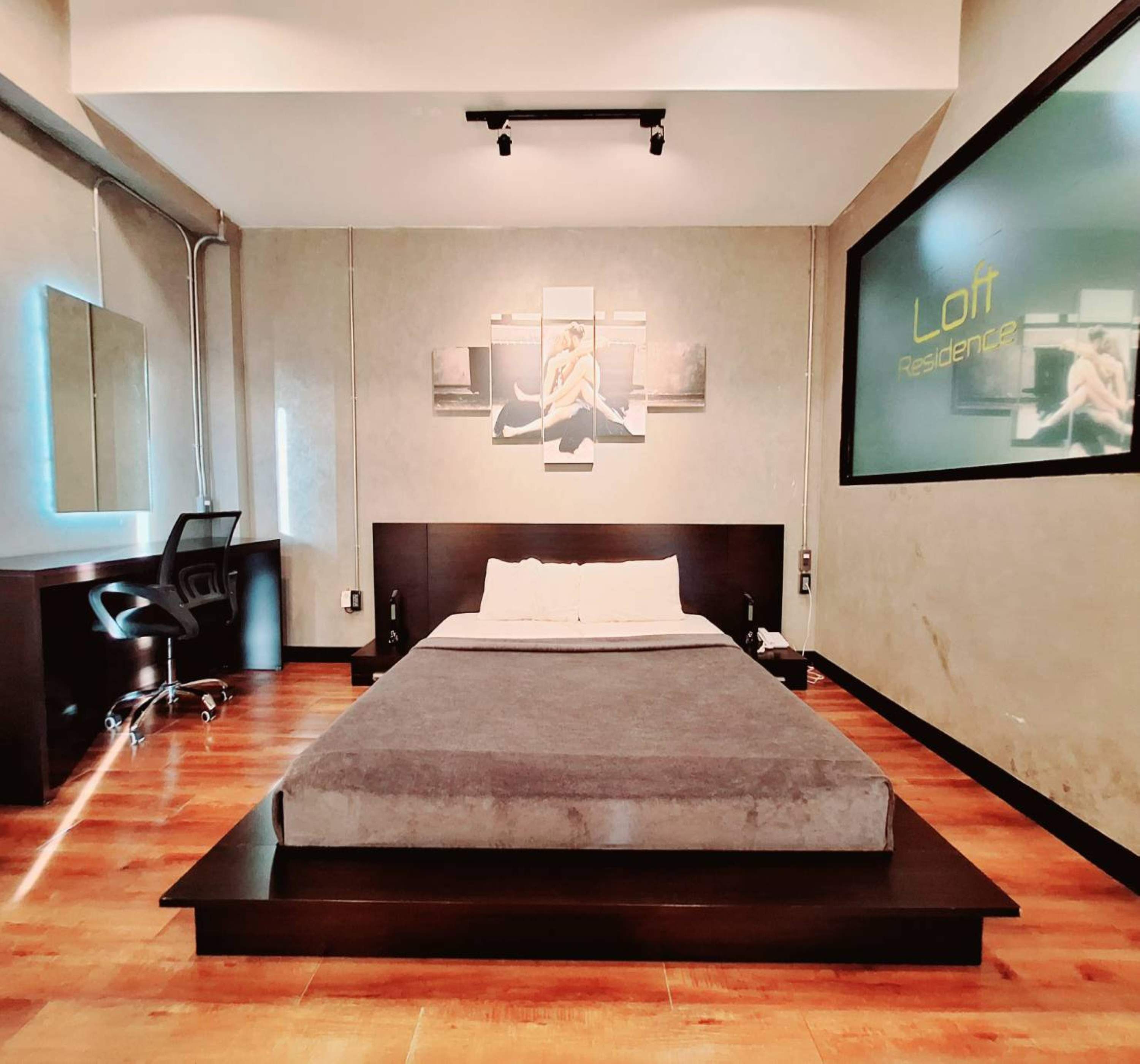 A modern bedroom with a large bed, a desk with a chair, and a large screen displaying 'Lott Residence'.