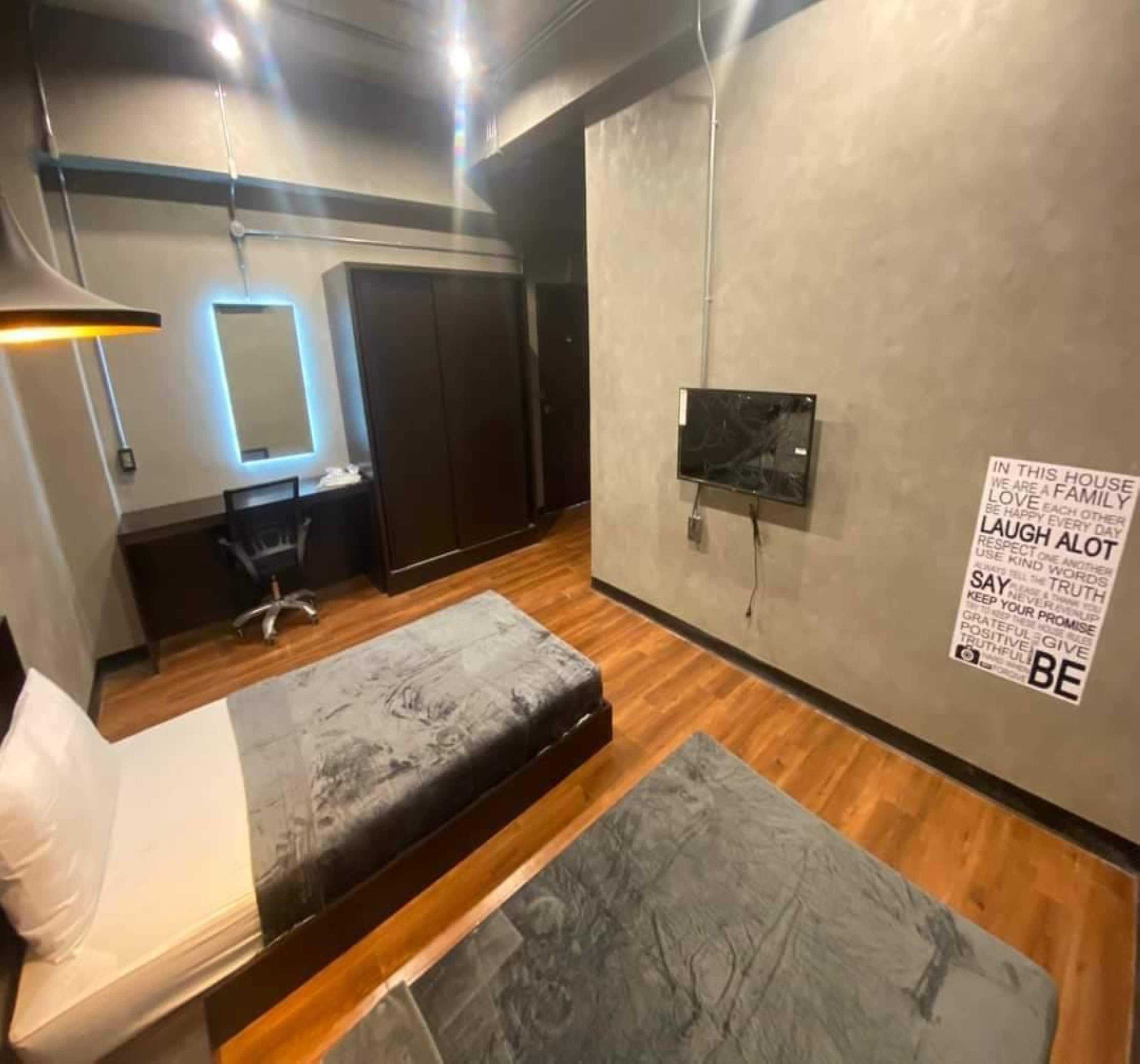 A modern bedroom with a bed, a desk, a chair, and a wall-mounted TV.