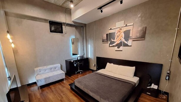 A modern bedroom with a large bed, a seating area, and a desk. - Capital O 75512 Loft Residence (Suphan Buri)