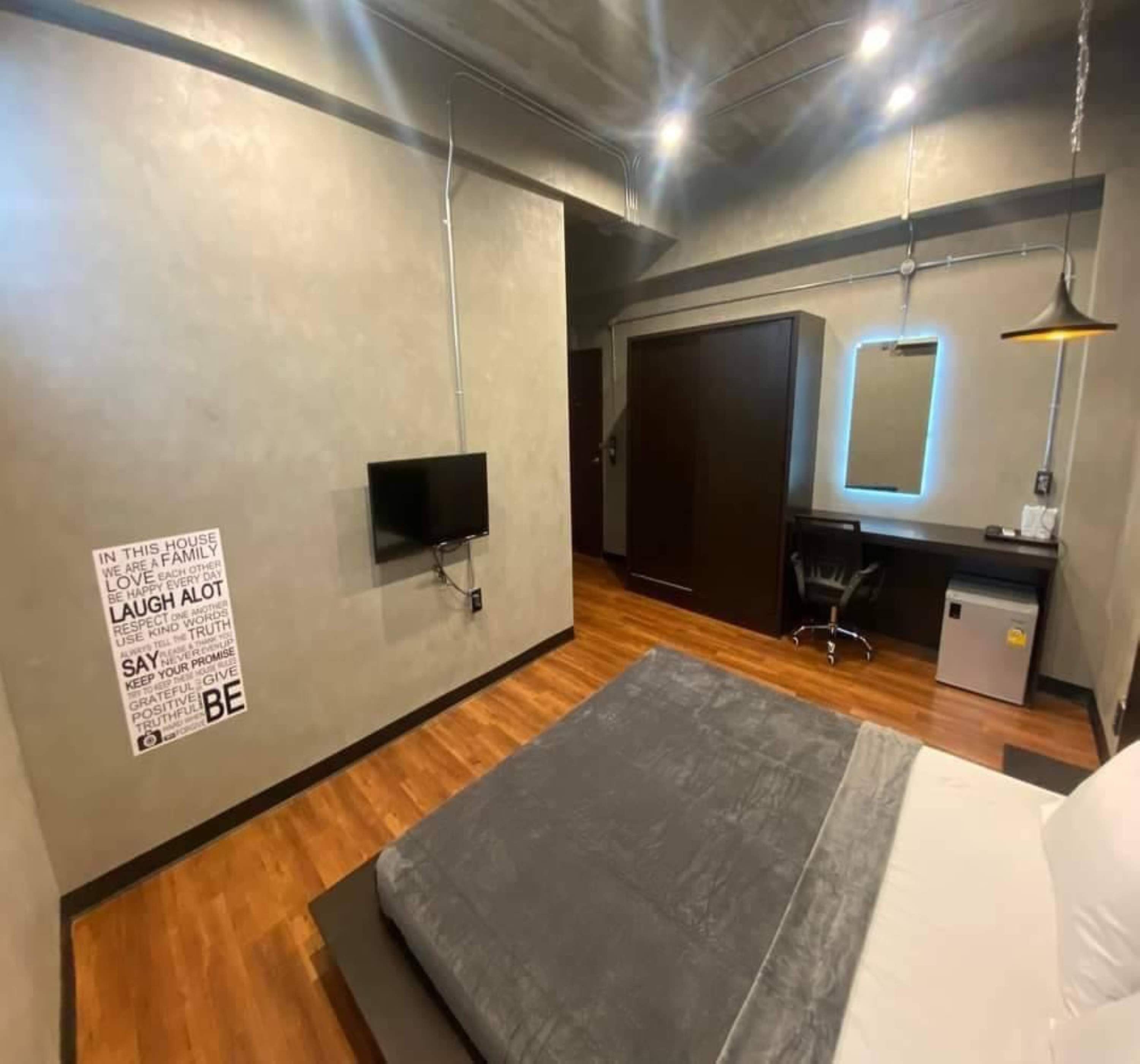 Una camera da letto moderna con un letto, una scrivania, una sedia, una TV e un poster motivazionale appeso al muro.