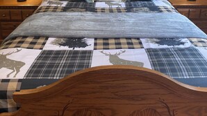 Una cama bien tendida con una colcha a cuadros y almohadas decorativas, flanqueada por mesitas de noche de madera con lámparas.