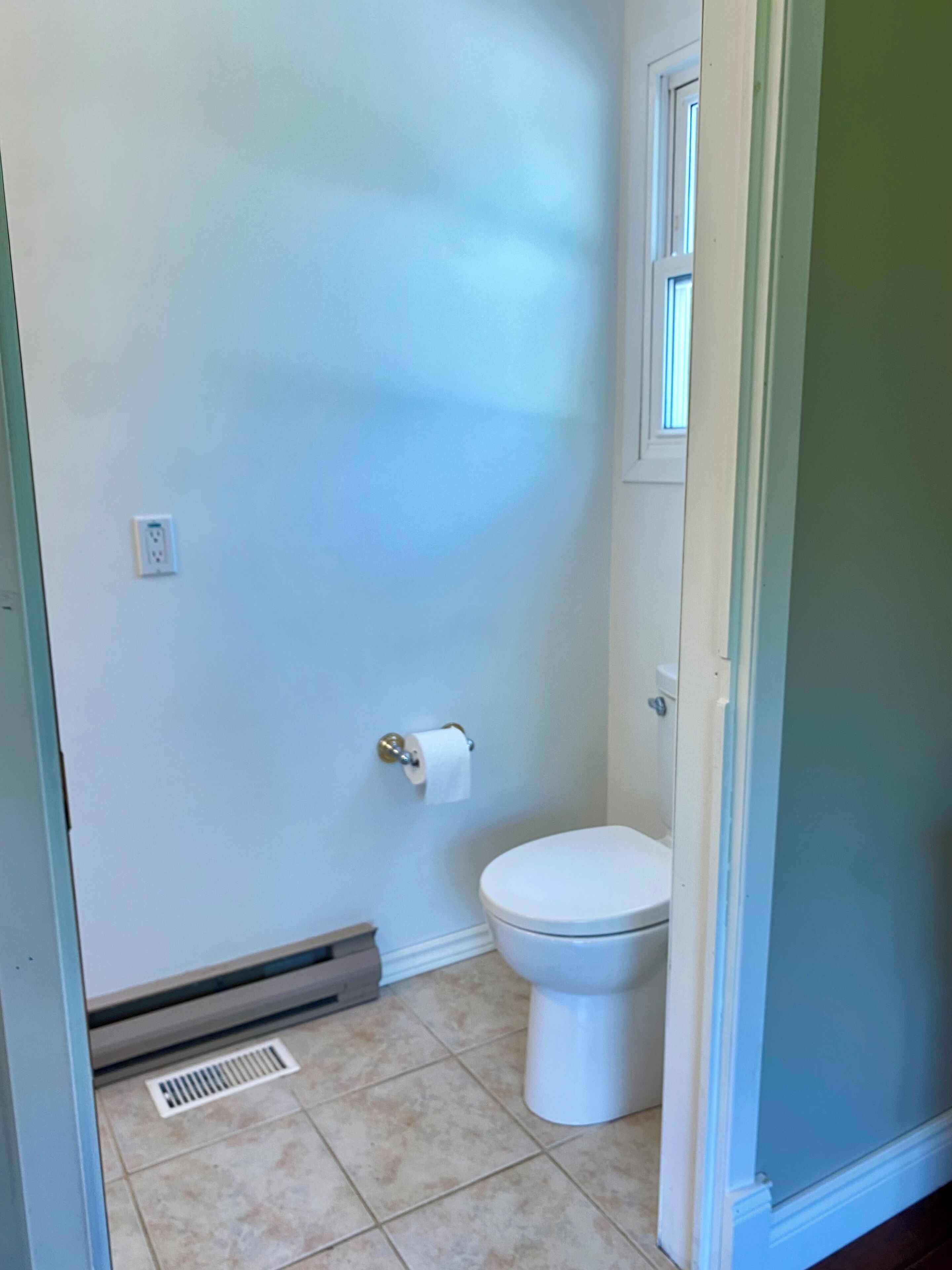 Ein Badezimmer mit Toilette, Toilettenpapier, Lüftung und Fußbodenentlüftung.