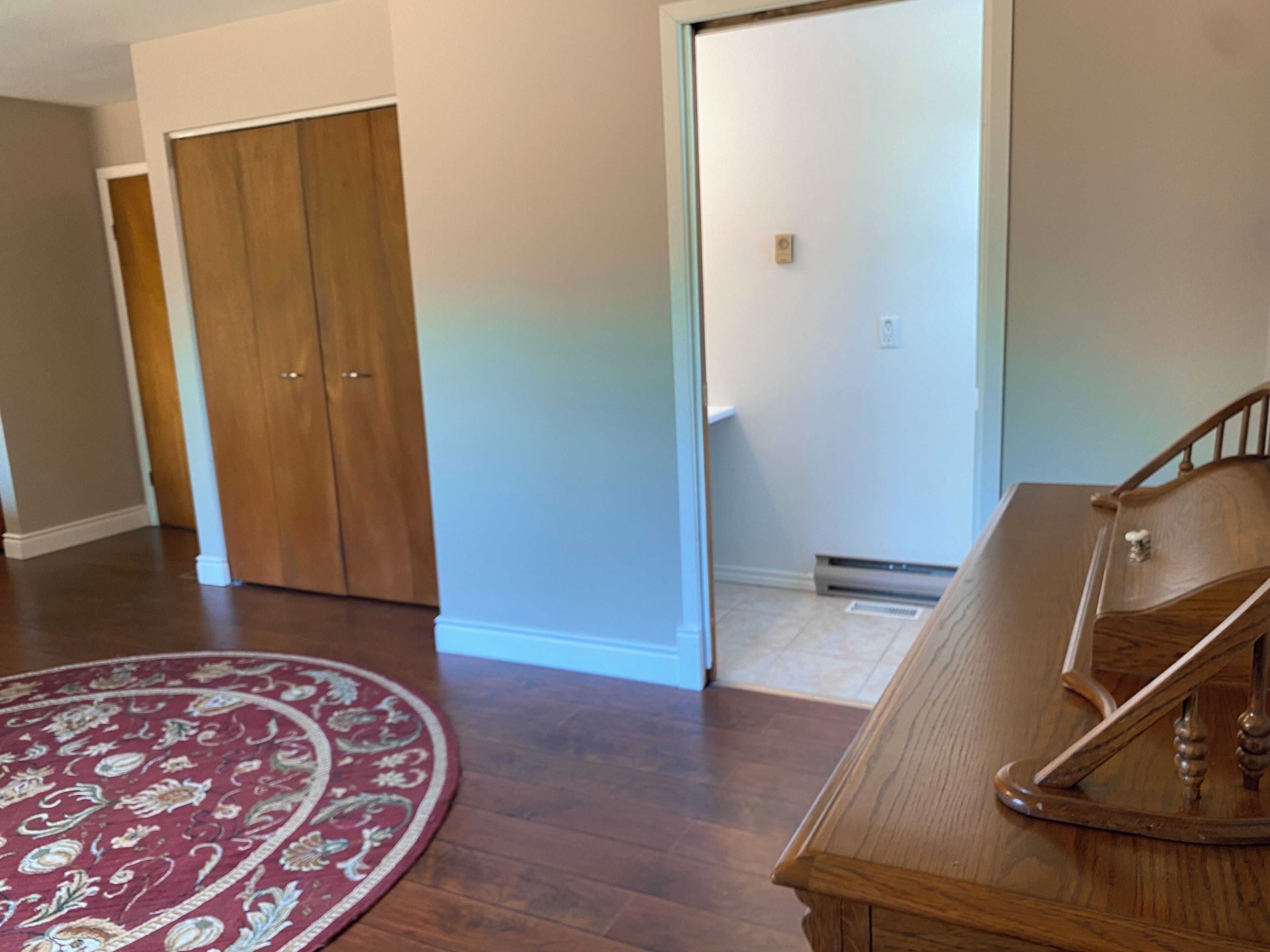 Une pièce avec un plancher en bois, un banc en bois, un tapis rouge à motifs et une porte coulissante.