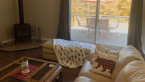 Una sala de estar acogedora con chimenea, un sofá con cojines estampados, una mesa de centro y vistas a una terraza exterior con sillas y una mesa.