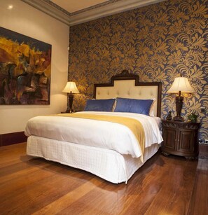 A bedroom with a large bed, two bedside lamps, a decorative headboard, a patterned wallpaper, and a painting on the wall. - The Orchids Hotel (Bogotá)