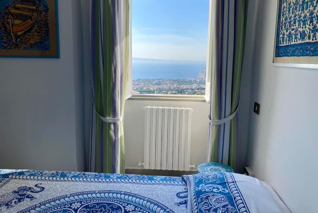 A bedroom with a bed, curtains, a radiator, and a view of a cityscape through a window.