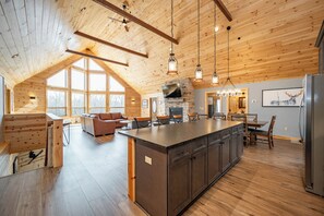 Une cuisine spacieuse avec un grand îlot central, des poutres apparentes en bois au plafond et une cheminée en pierre.