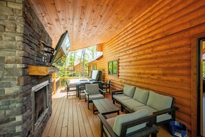 A log cabin with a fireplace, outdoor seating area, and a view of the surrounding forest.