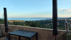 Un balcon avec une table et des chaises, donnant sur une ville côtière et la mer.