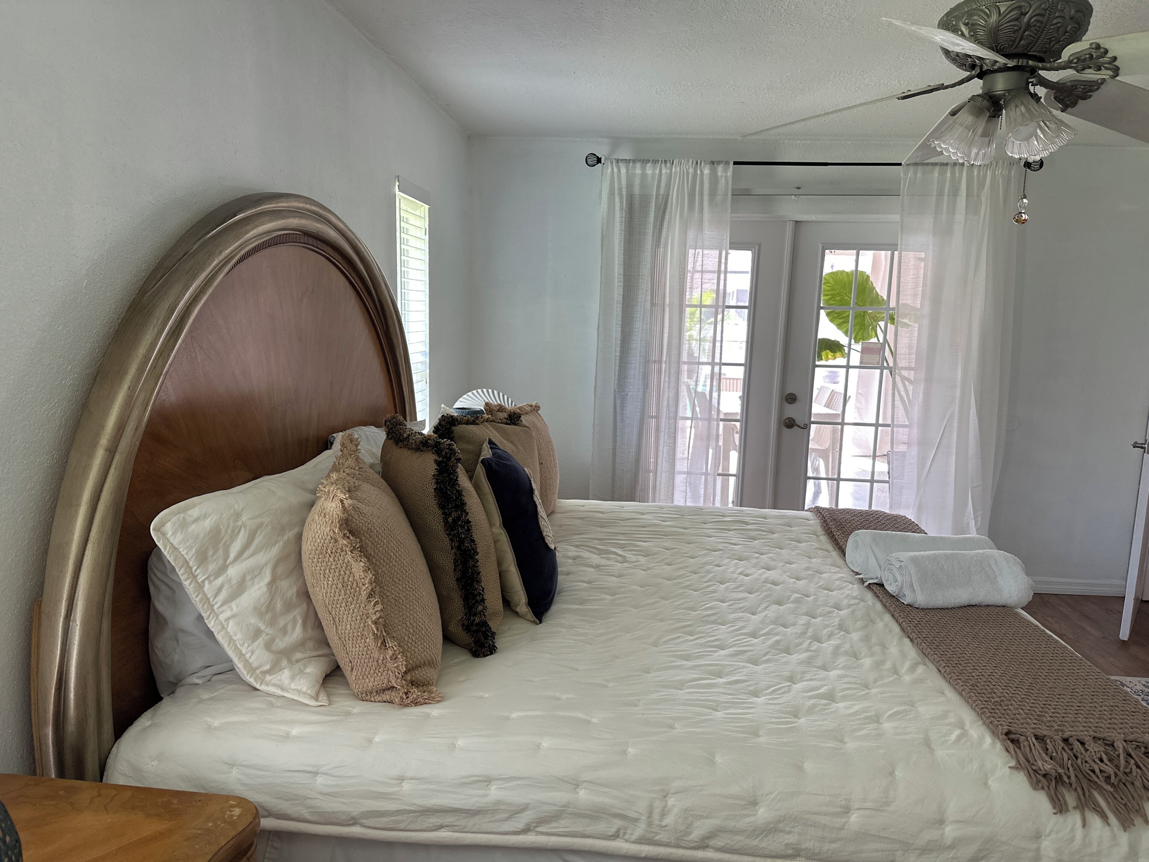 A bedroom with a large bed, a ceiling fan, and a view of the outdoors through a door.