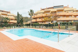 A swimming pool with tiled deck, surrounded by a fence, and adjacent to a residential building with balconies.