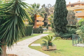 A pathway leading to a building with a yellow facade, surrounded by well-maintained greenery and a tall evergreen tree. - Sky Sea Holidays Mijas Costa (Mijas)