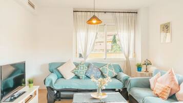 Un salon avec un canapé de couleur turquoise, une table basse, un téléviseur et une fenêtre avec des rideaux.