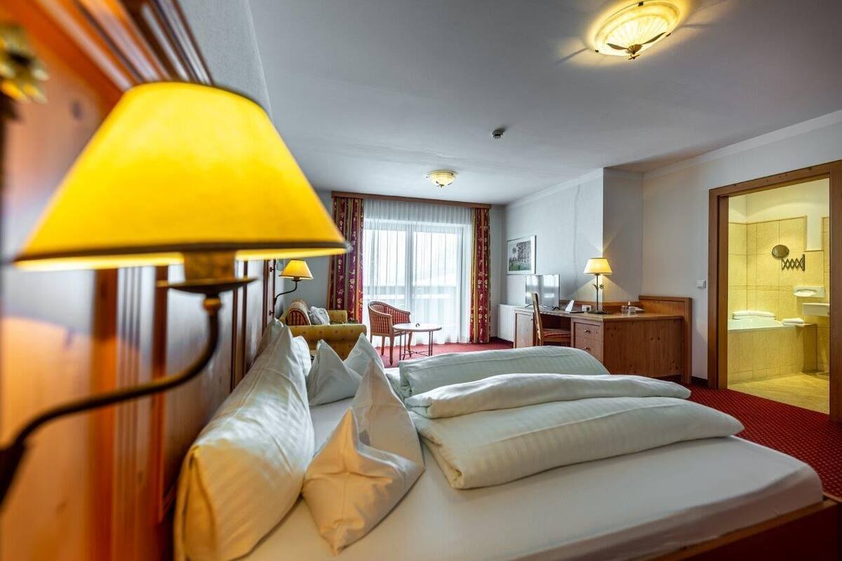 Camera d'albergo con un letto, due lampade ai lati del letto, una scrivania, una sedia e un bagno visibile attraverso una porta aperta.
