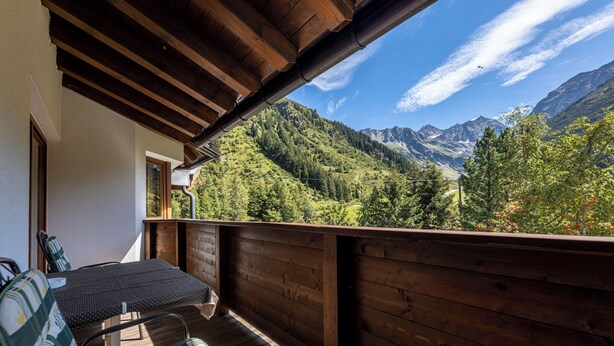 A wooden deck with a table and chairs, overlooking a mountainous landscape. - Hotel Gletscherblick (Sankt Leonhard im Pitztal)