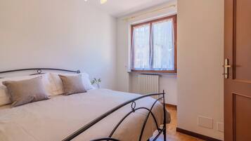 Un dormitorio con cama, una ventana con cortinas, un radiador y una puerta de madera.