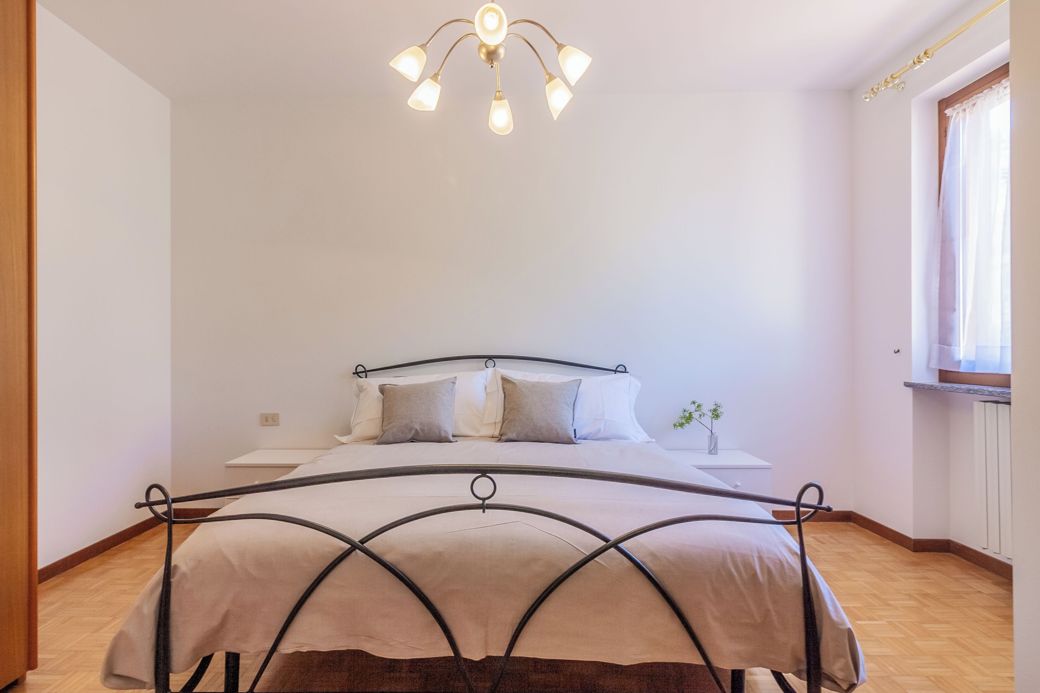 Une chambre à coucher comprenant un lit, des tables de chevet, un luminaire au plafond et une fenêtre avec des rideaux.