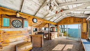 A rustic wooden cabin with a wooden deck, a dartboard, a clock, and a view of the sea. - Redwood Retreat Waterfront Cottage By Simcoe With Hot Tub And Sauna (Orillia)