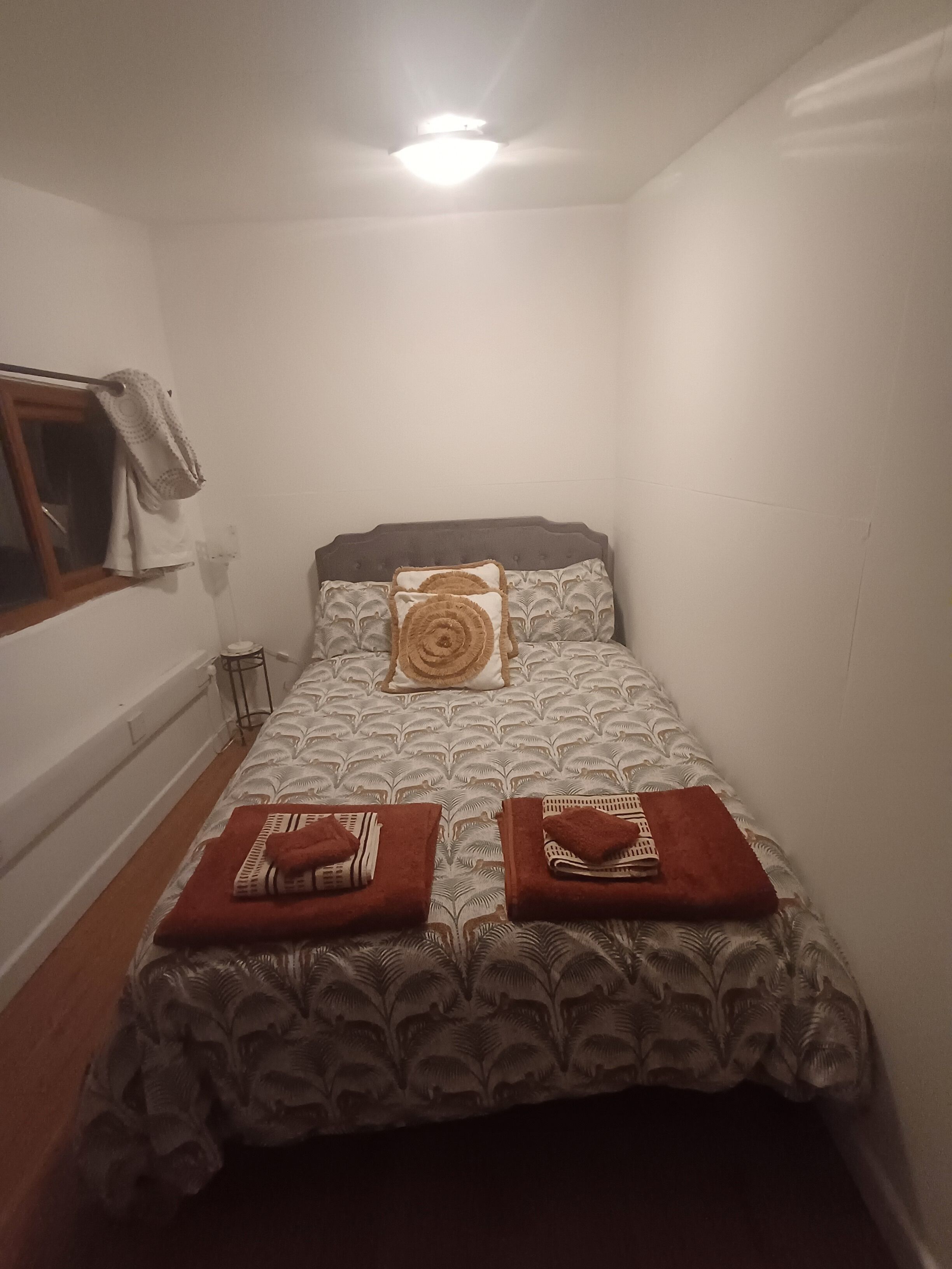 A small, neatly made room with a single bed, a window with curtains, and a ceiling light.