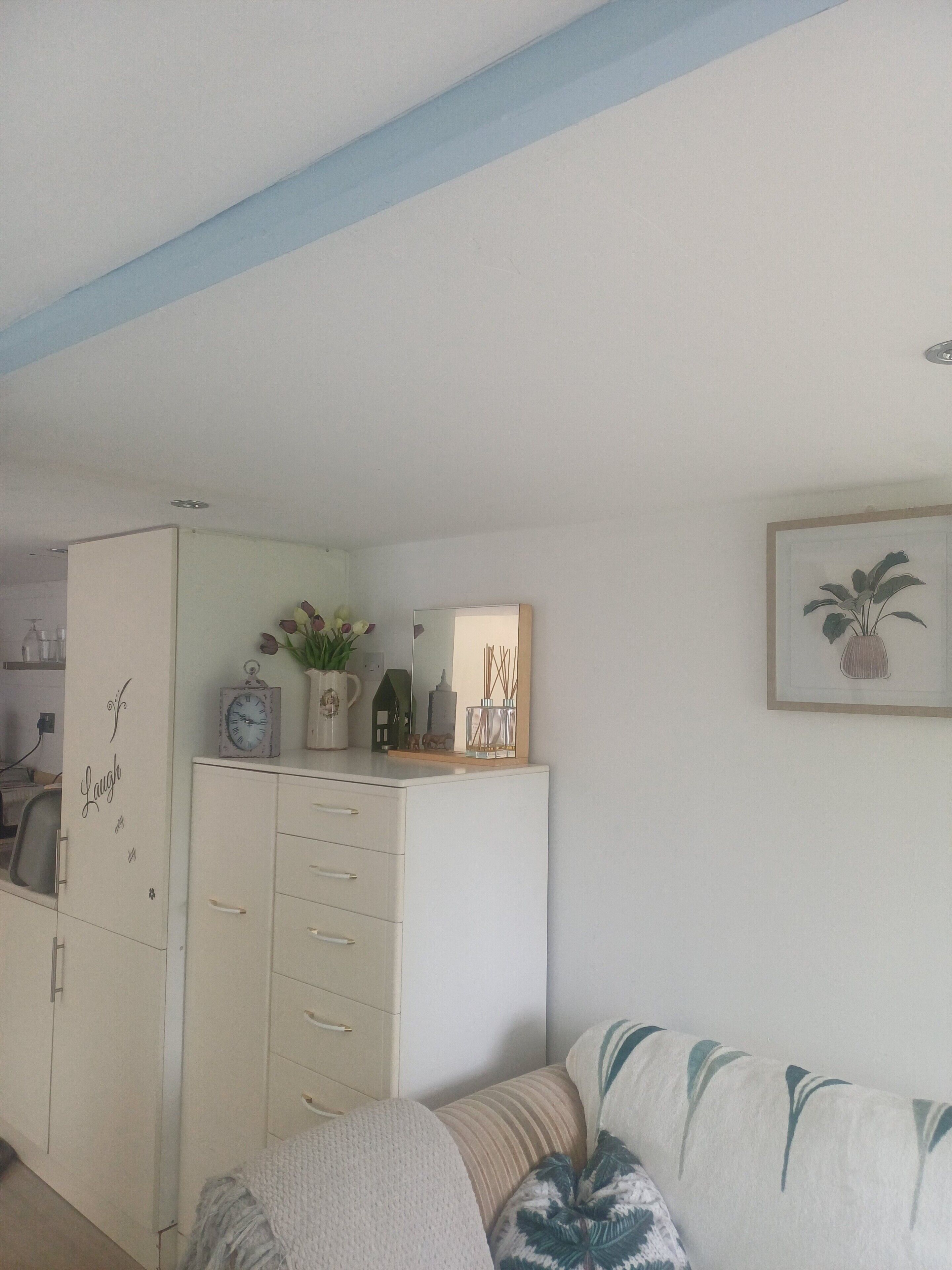 A living room with a sofa, a cabinet with drawers, a clock, a potted plant, and a framed picture on the wall.