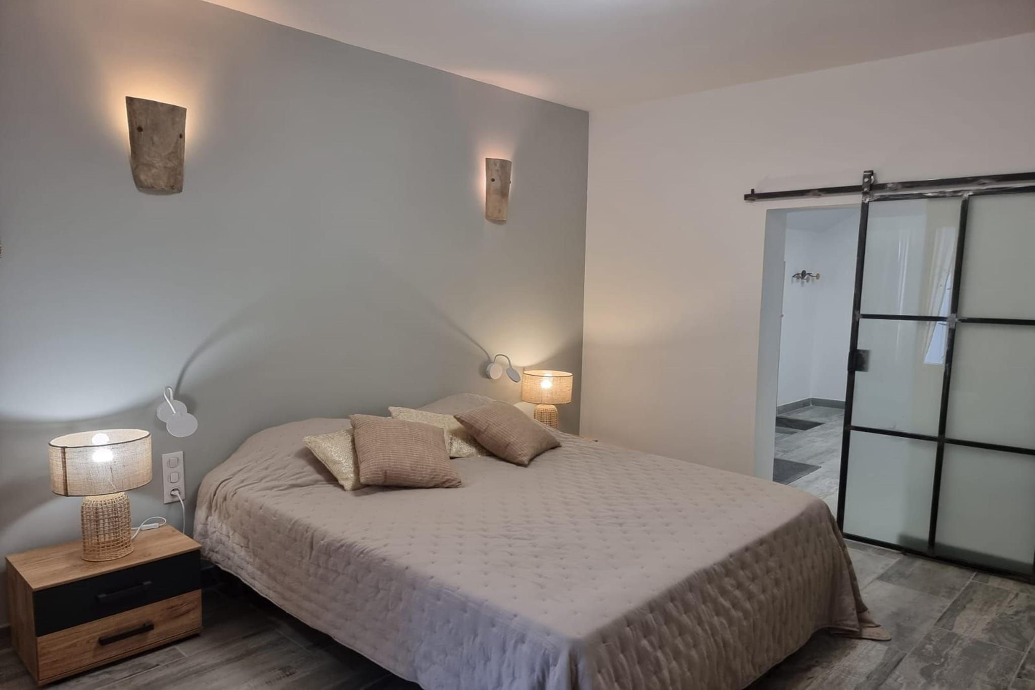 Un dormitorio con cama, lámparas de noche, mesita de noche y puerta corrediza de vidrio.