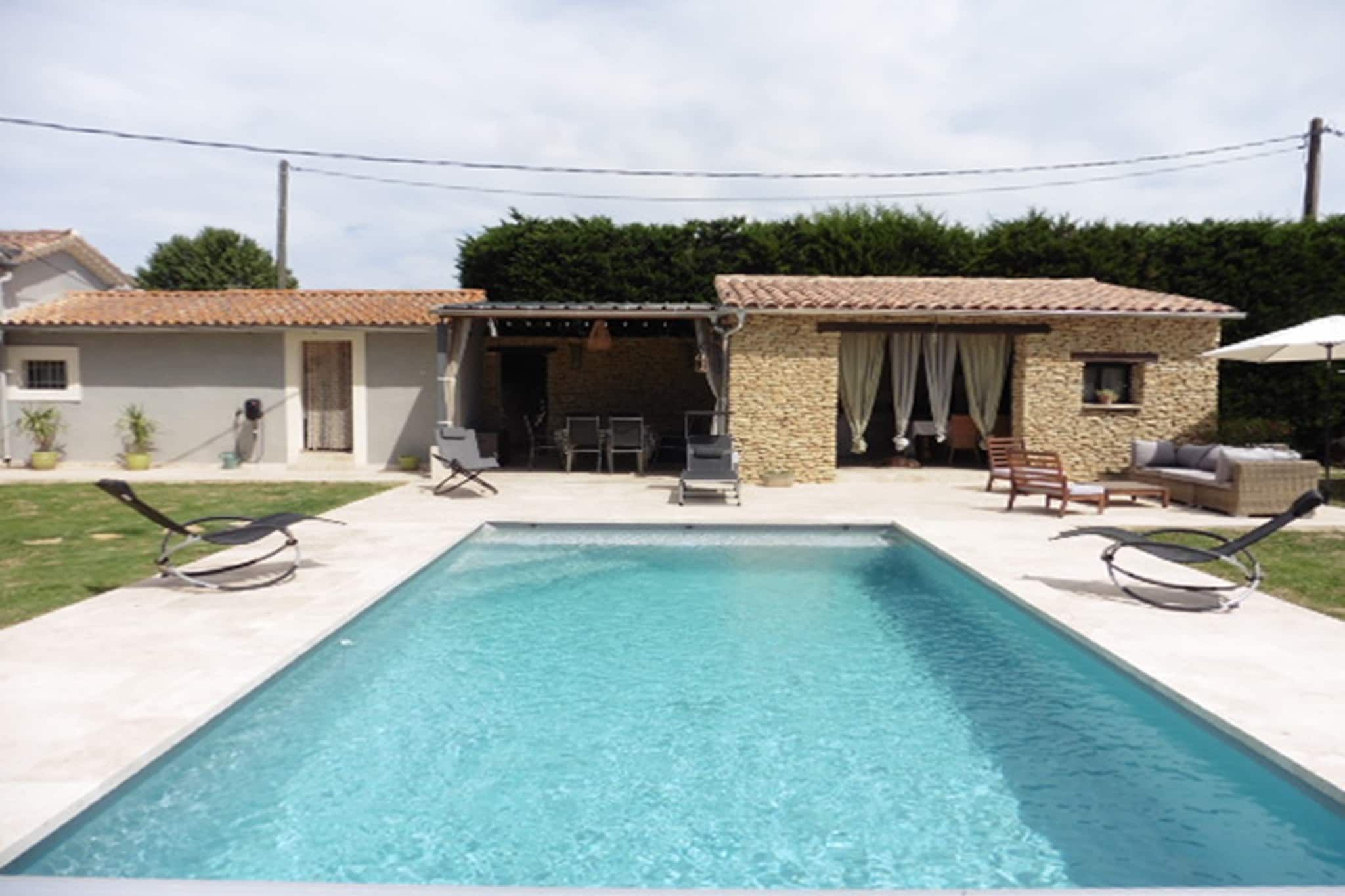 A rectangular swimming pool with lounge chairs and a stone building with a tiled roof in the background.