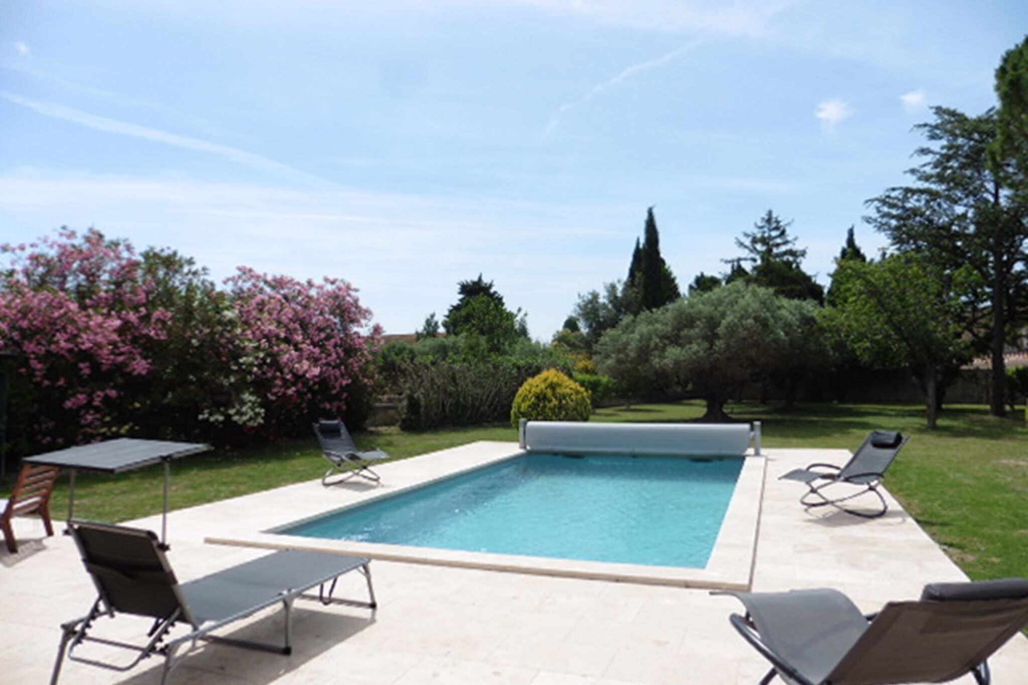 A rectangular swimming pool with a tiled deck, surrounded by lounge chairs and a table.