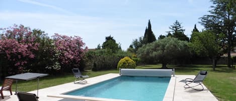 A rectangular swimming pool with a tiled deck, surrounded by lounge chairs and a table.