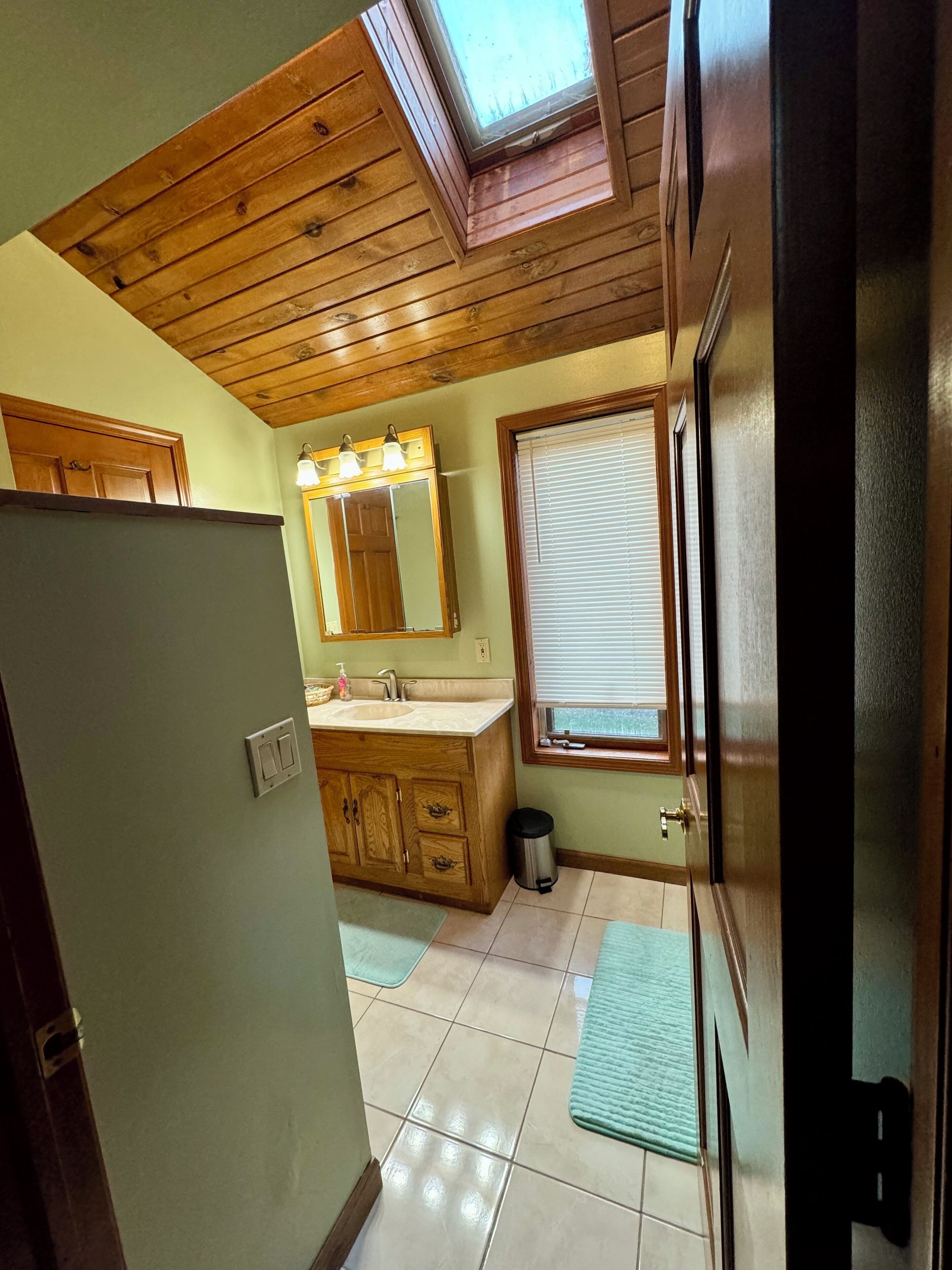 A bathroom with a wooden vanity, a sink, a mirror, and a window with blinds.