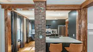 Una cocina moderna con una isla central, dos taburetes de bar y una pared decorativa de ladrillo.