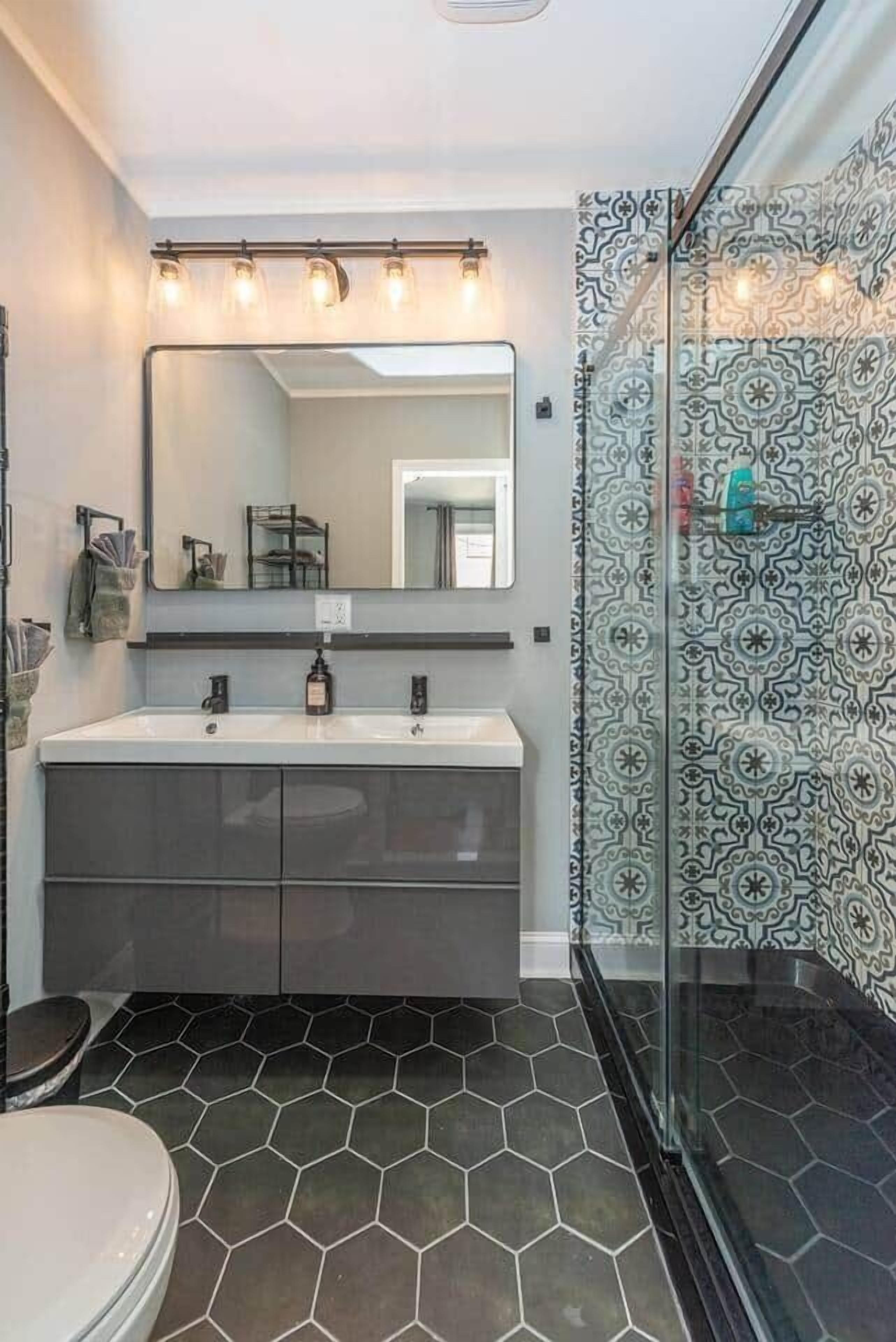 Une salle de bain avec un meuble-lavabo à deux vasques, un grand miroir et une douche aux carreaux décorés.