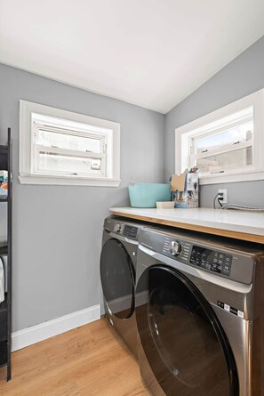 Une buanderie équipée d’un lave-linge et d’un sèche-linge à chargement frontal, d’un plancher en bois et d’une fenêtre donnant sur l’extérieur.