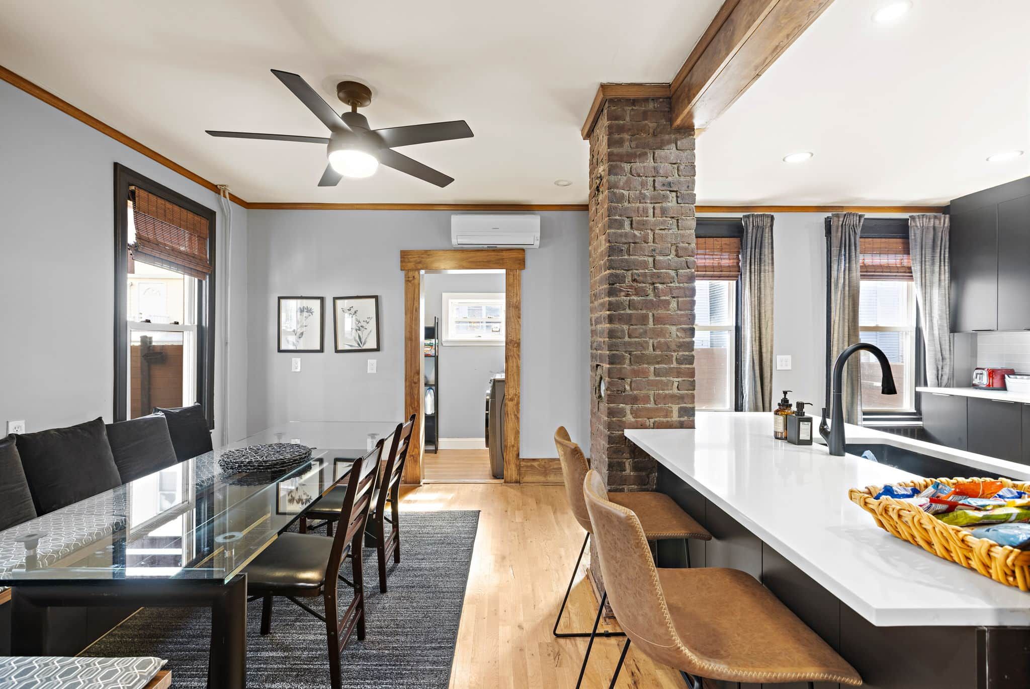 A modern kitchen with a central island, a dining area with a glass table, and a ceiling fan.