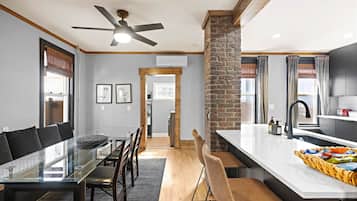 A modern kitchen with a central island, a dining area with a glass table, and a ceiling fan.