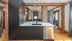 Una cocina moderna con una isla central, vigas de madera y una pared de ladrillo decorativa.