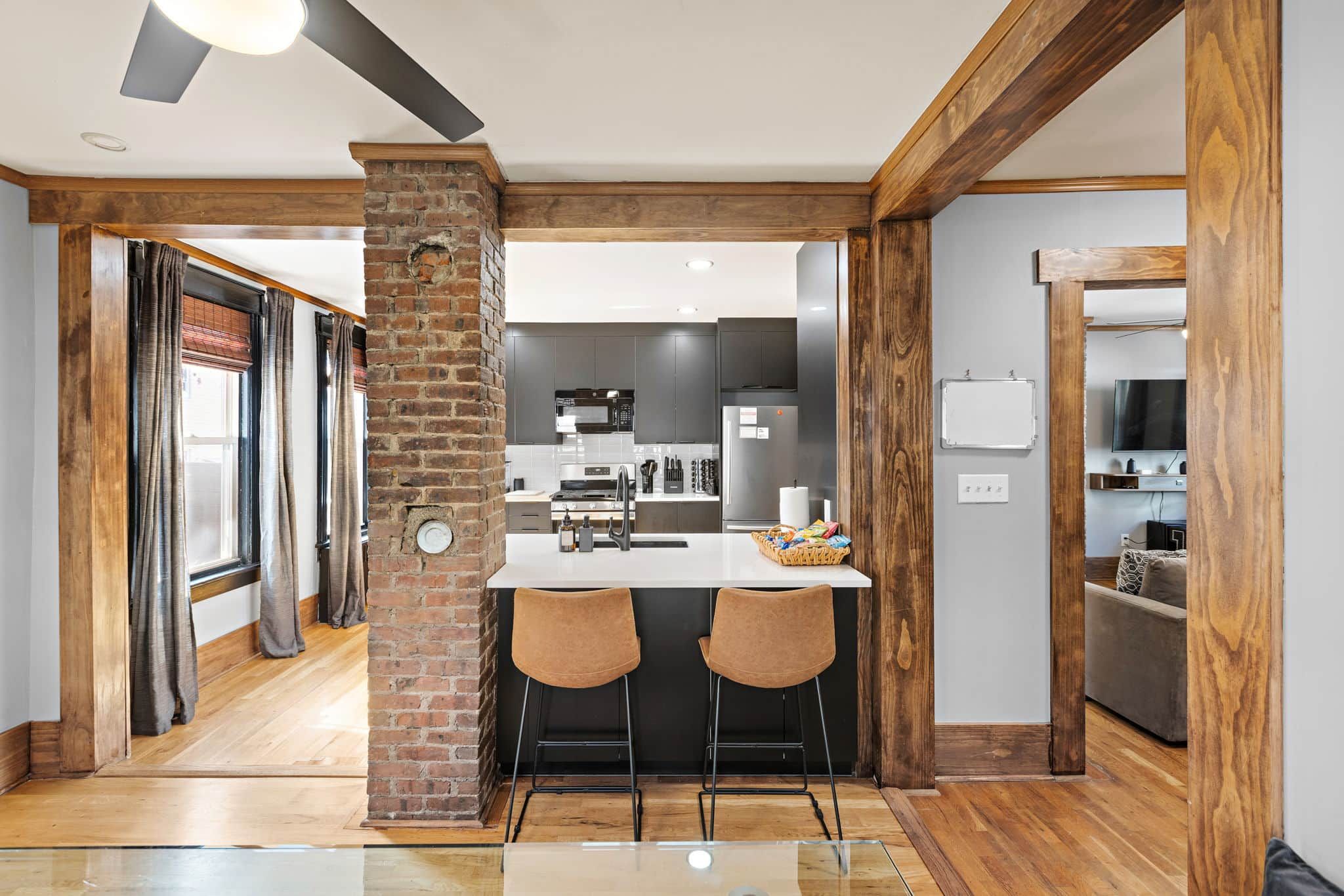 Une cuisine moderne avec un îlot central, deux tabourets de bar et une colonne en briques.