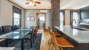 Una cocina moderna con una isla central, un comedor con mesa de vidrio y una escalera que sube a otro nivel.