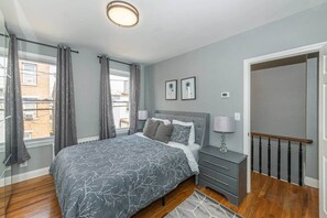 Ein Schlafzimmer mit Bett, Nachttischen, einer Lampe und einem Fenster mit Vorhängen.