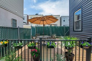 Eine Terrasse mit Tisch und Stühlen, umgeben von einem schwarzen Metallzaun und Kübelpflanzen.