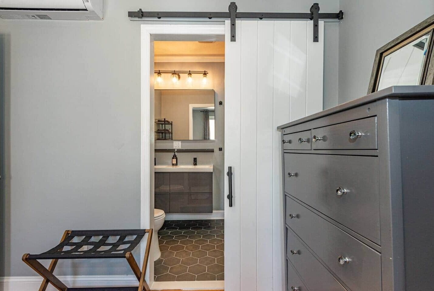 Une salle de bain moderne avec un meuble-lavabo blanc, un grand miroir et un sol carrelé de motifs hexagonaux.