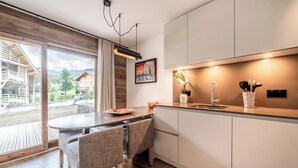 Eine moderne Küche mit Essbereich, Holzboden und Blick auf ein Holzhaus und Grünfläche im Freien.
