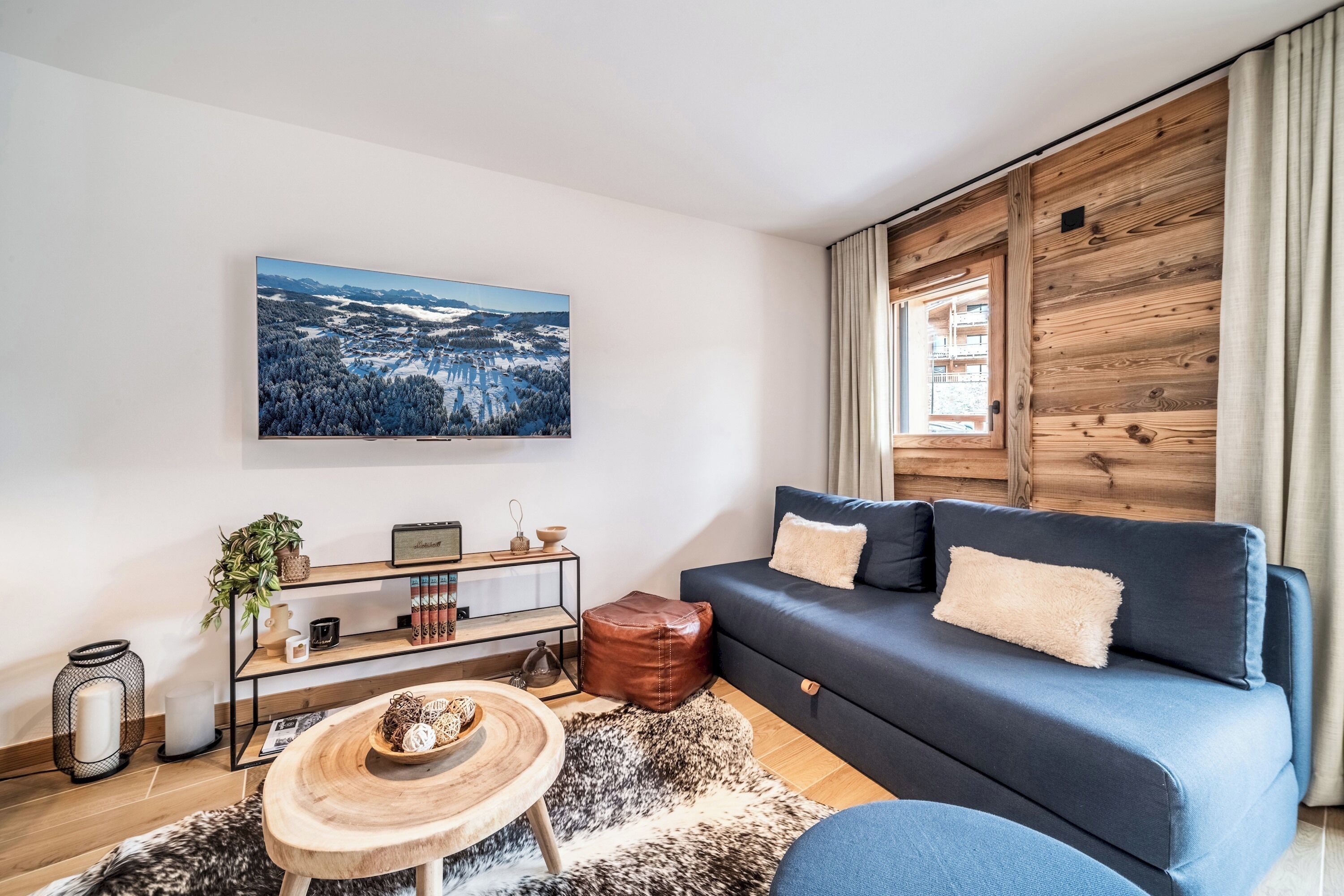 A modern living room with a dark blue sofa, a wooden coffee table, a large painting of a snowy landscape, and a wooden accent wall.