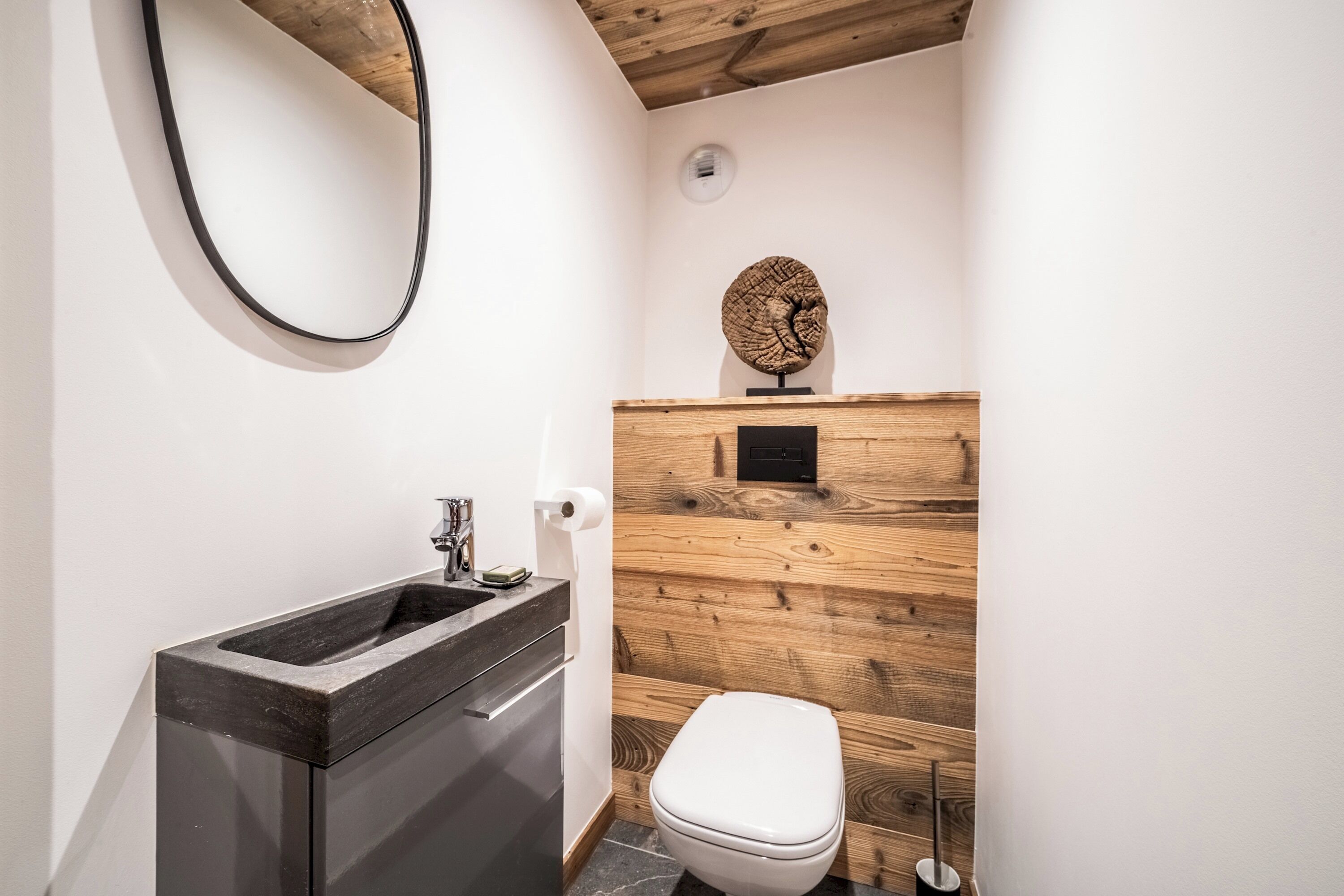 Een moderne badkamer met een houten wandpaneel, een zwarte wastafel en een wit toilet.