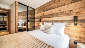 Ein Schlafzimmer mit einer Holzwand, einem Bett mit weißer Bettwäsche und einer Schiebetür zu einem anderen Raum.