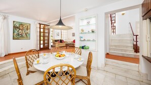 A dining area with a round table, wicker chairs, a hanging light fixture, and a staircase leading to an upper floor. - Villa Mexico - Four Bedroom Villa, Sleeps 8 (Quarteira)