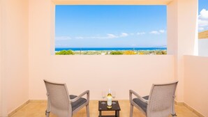 A balcony with two wicker chairs, a small table with a bottle of wine and two glasses, and a view of the sea and landscape. - Villa Maia - Three Bedroom Villa, Sleeps 6 (Rhodes)